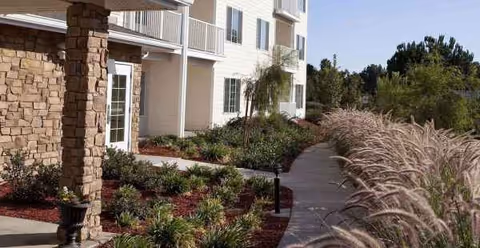Exterior view of Holiday Golden Oaks with a landscaped walkway beside a beige building.