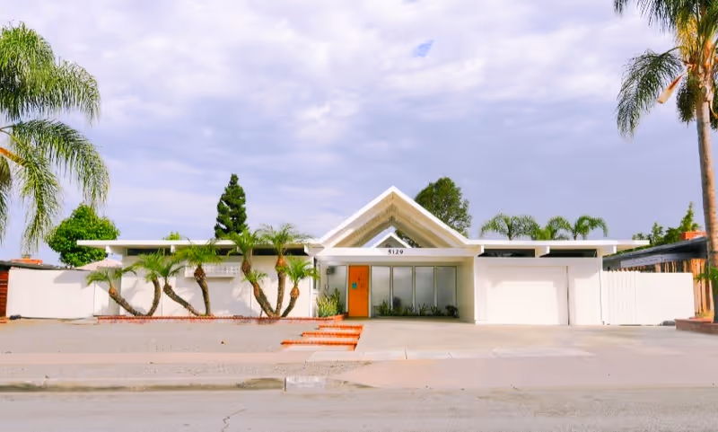 Front exterior of a single-story facility with a triangular roof, glass doors, and palm trees.