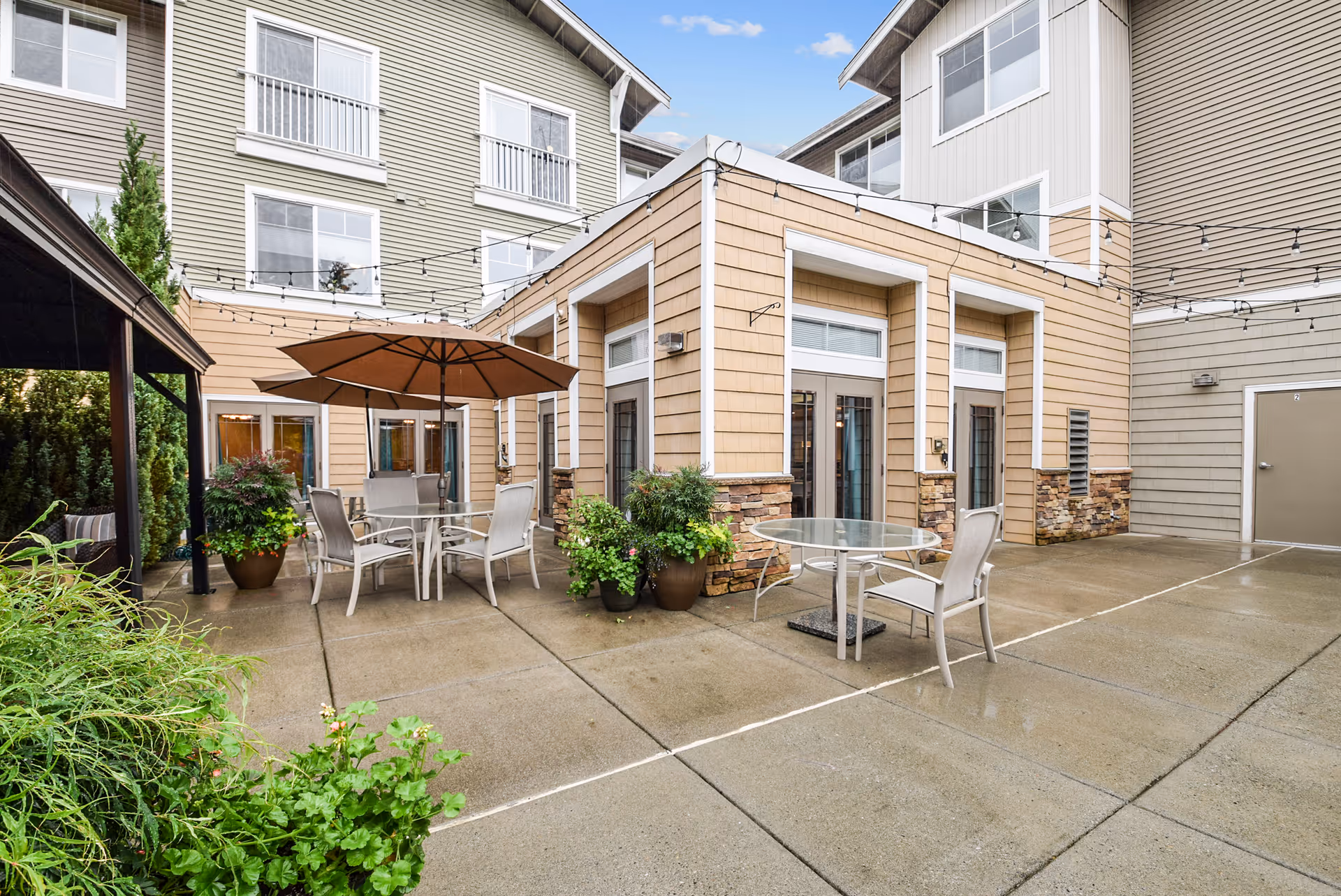 Outdoor courtyard patio with tables, chairs, an umbrella, and potted plants beside the Woodland Terrace building.