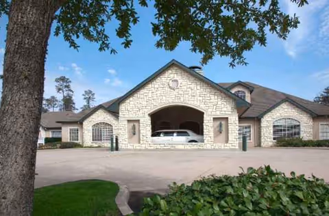 Stone-facade senior living facility with a white car parked in a central arched garage entrance.