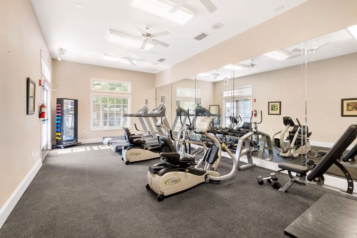Bright fitness room with treadmills, recumbent bikes, free weights and a mirrored wall.