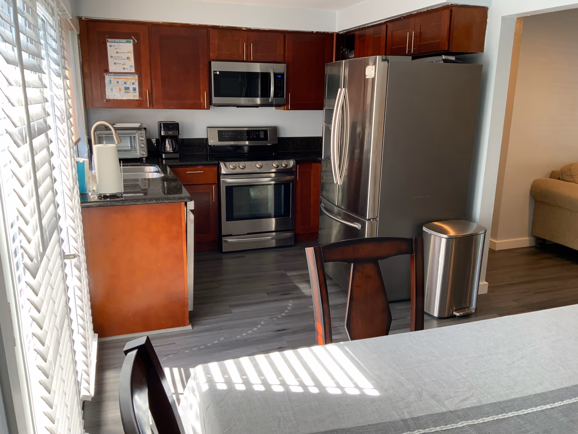 Modern kitchen with stainless steel appliances, dark wood cabinets, and a dining table in the foreground.