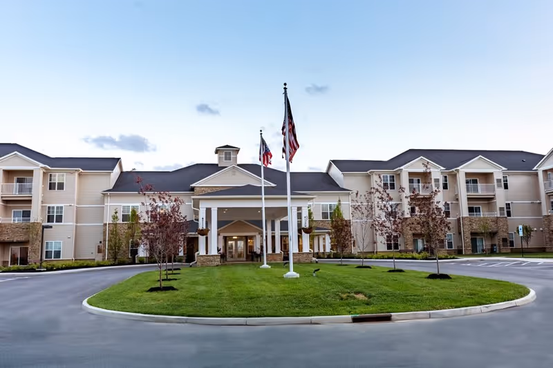 Front exterior view of StoryPoint Grove City facility with a circular driveway, green lawn, small trees, and three flagpoles displaying flags in front of the building entrance.