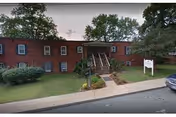 Brick senior living building with stairs and a grassy front yard.