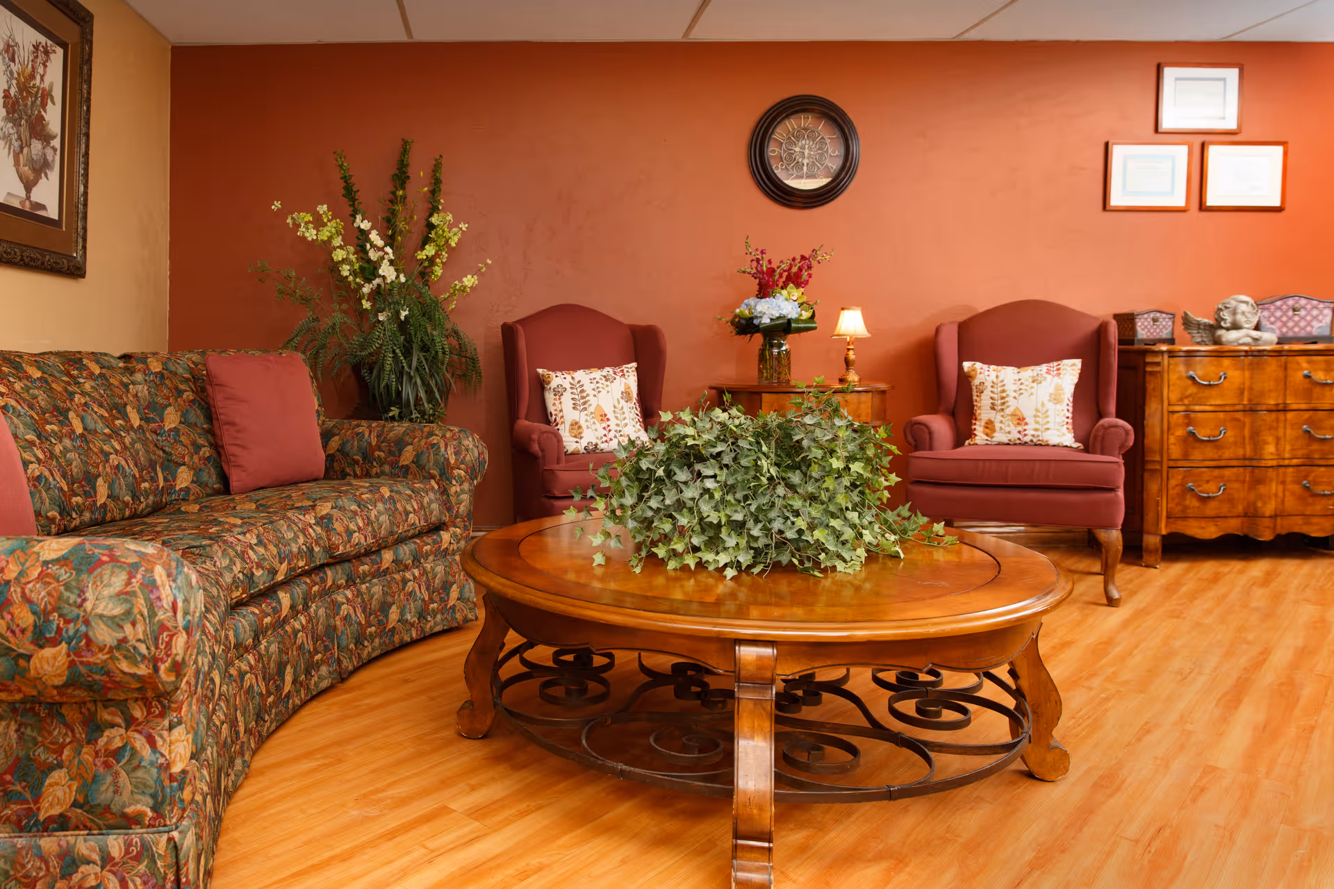 Cozy seating area with a patterned sofa, two armchairs and a wooden coffee table topped with a leafy centerpiece in a warmly decorated room.