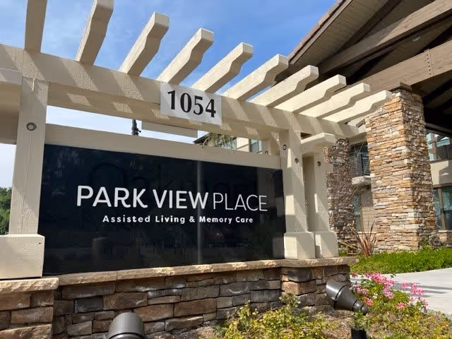 Outdoor entrance sign reading 'PARK VIEW PLACE Assisted Living & Memory Care' beneath a pergola with the address 1054 and landscaped foreground.