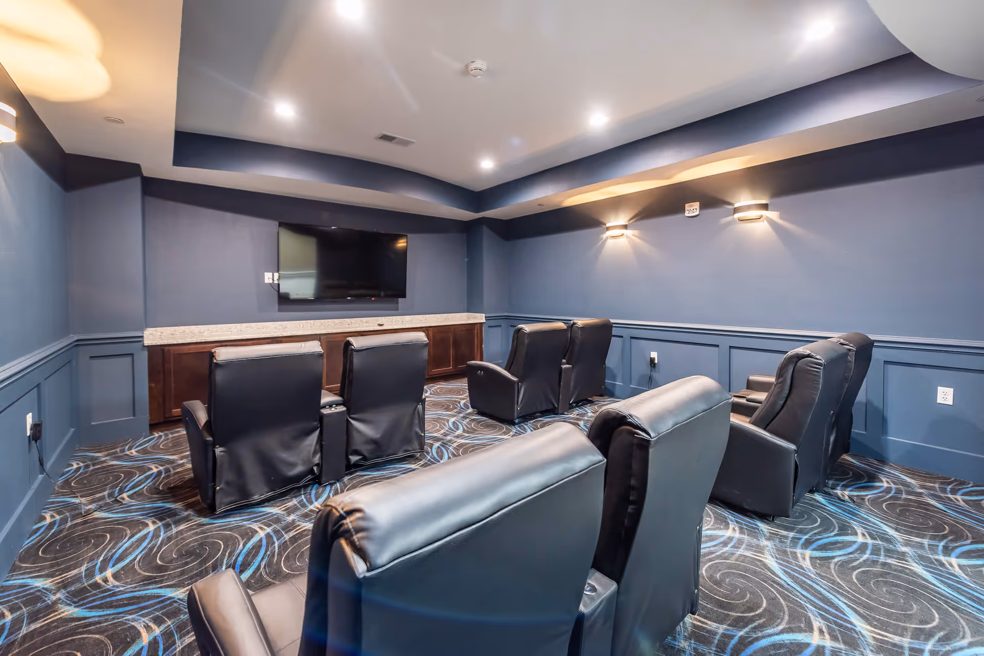 Small private theater room with rows of black leather recliners facing a wall-mounted TV.