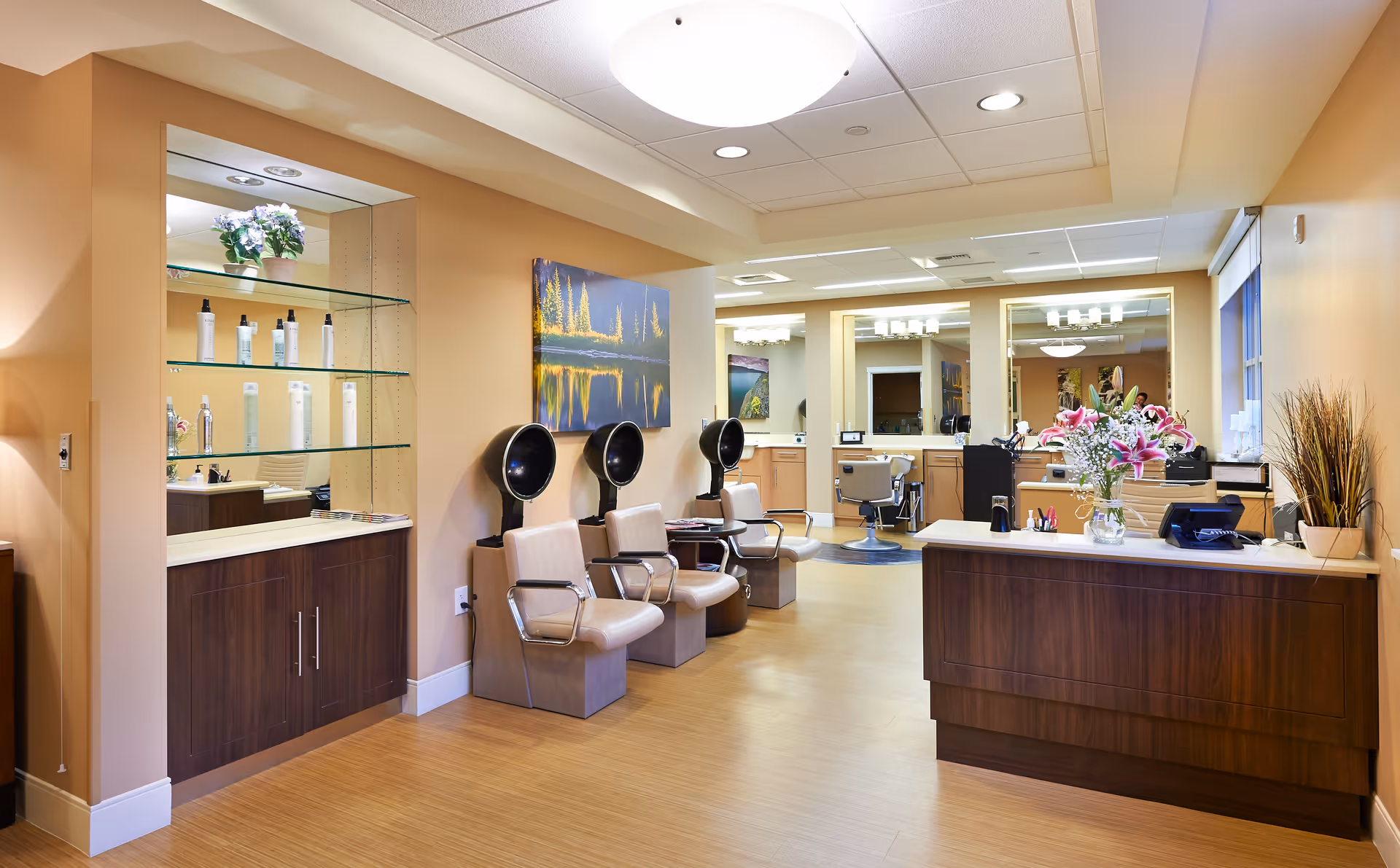 Bright salon interior with styling stations, hooded hair dryers, chairs, and a reception desk with flowers.