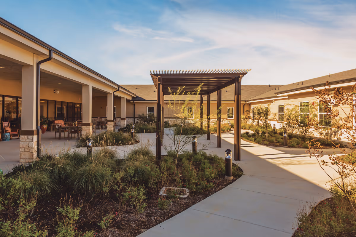 Courtyard with a pergola and covered walkway between single-story buildings, landscaped planting beds and outdoor seating.