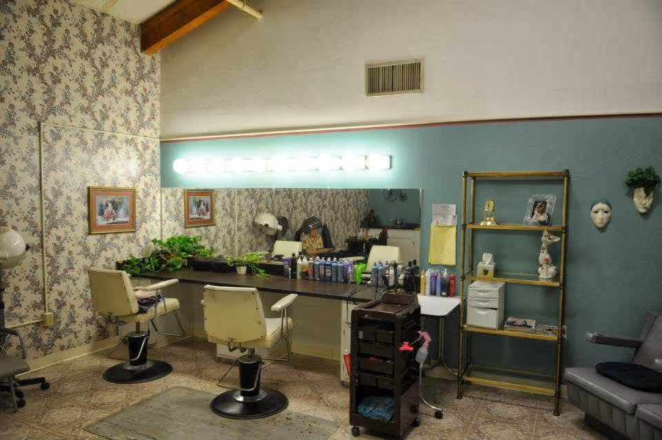 Interior salon area with styling chairs, a large mirror, hair products on a countertop and shelving against floral wallpaper.