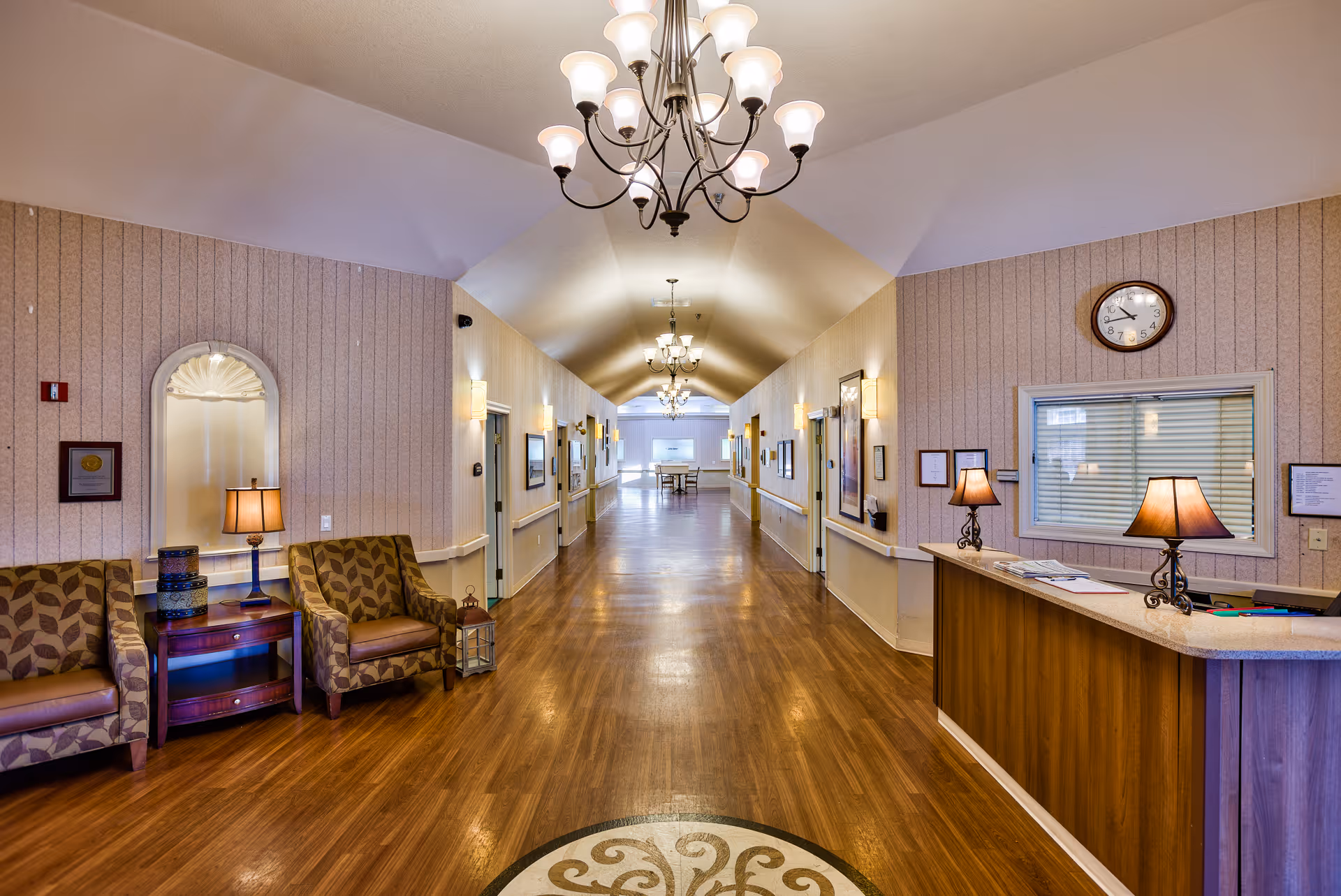 Reception desk and seating area opening onto a long, well-lit hallway with chandeliers.