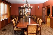 Formal dining room with a long wooden table, upholstered chairs, chandelier and a china cabinet against warm red walls.
