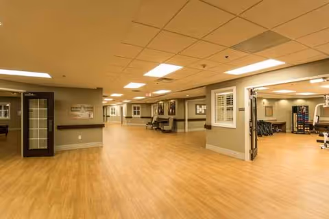 A large, empty senior living facility common area with wood floors and bright overhead lighting.