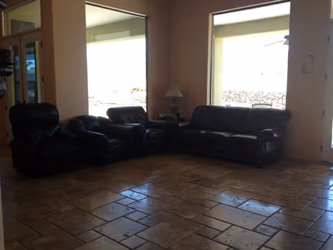 Spacious living room with dark leather sofa and armchairs arranged near large windows over a tiled floor.