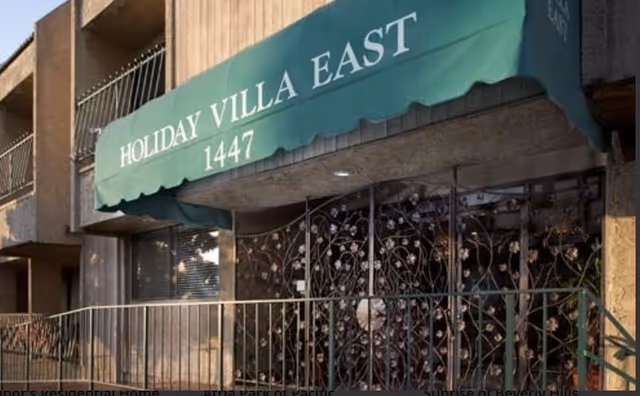 Green awning reads Holiday Villa East above a gated building entrance.