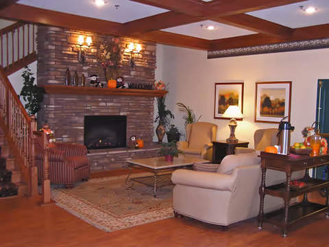 Cozy communal living room with a stone fireplace, upholstered chairs and sofa, coffee table, rug, and decorative accents.