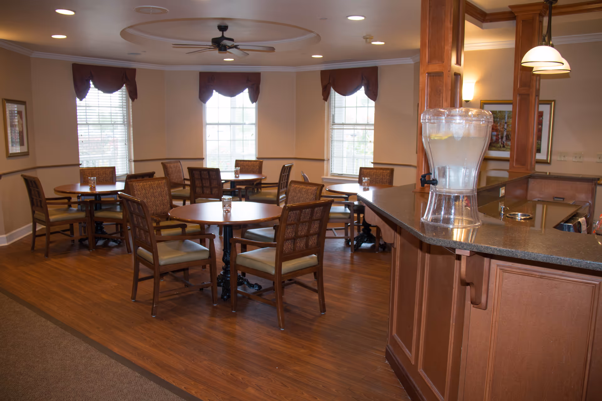 Dining room with round tables and chairs, hardwood floors, windows, and a countertop holding a water dispenser.
