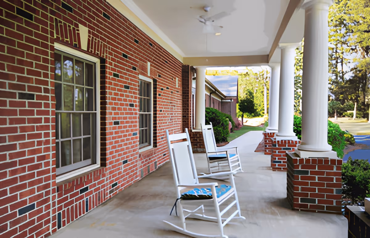 Covered brick front porch with white columns and rocking chairs overlooking a walkway and lawn.