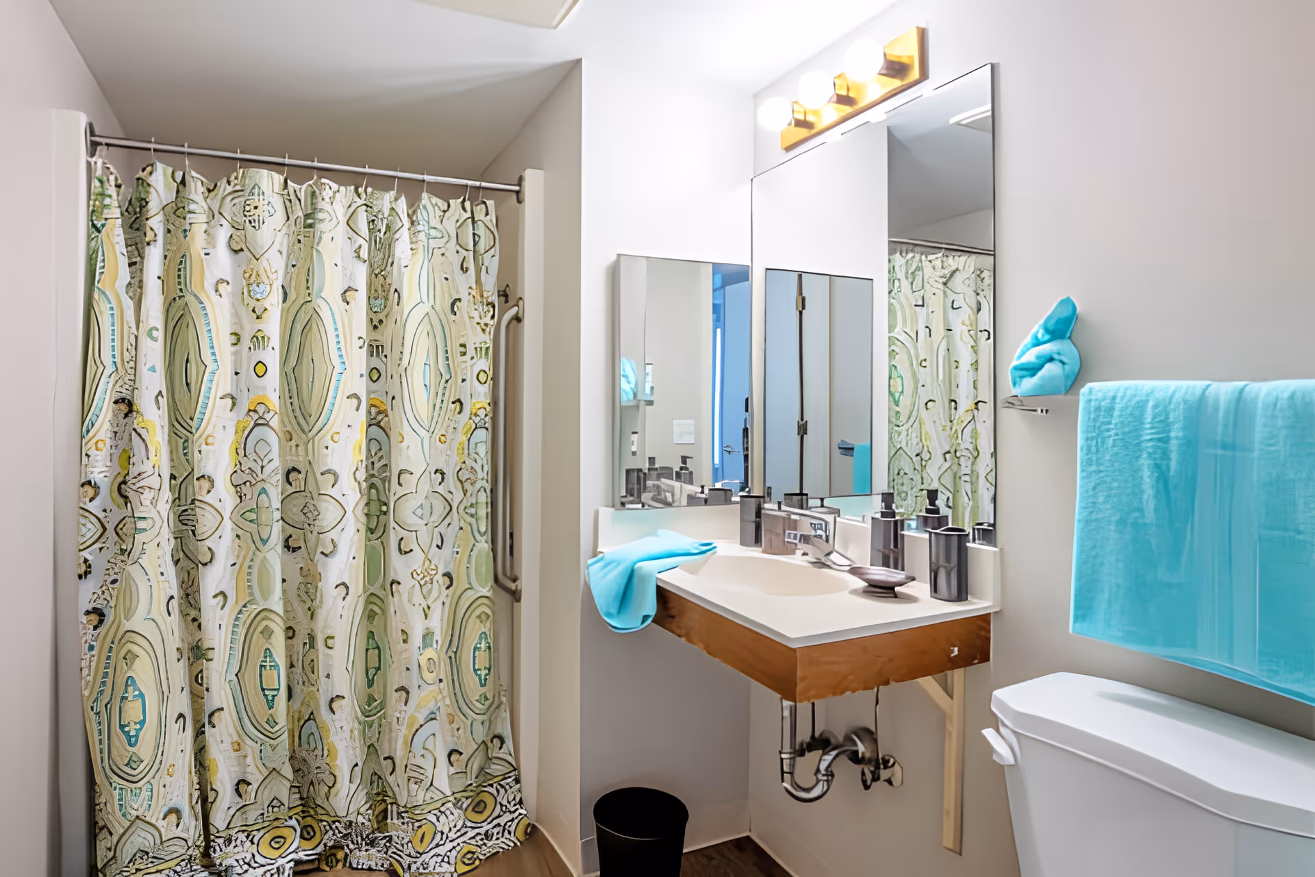 Bathroom with a patterned shower curtain, wall-mounted sink and mirror, and turquoise towels.