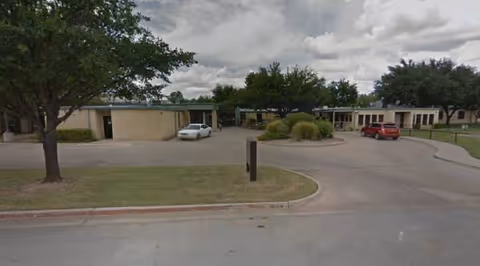Exterior view of Glen Rose Nursing and Rehab Center with a curved driveway and trees.