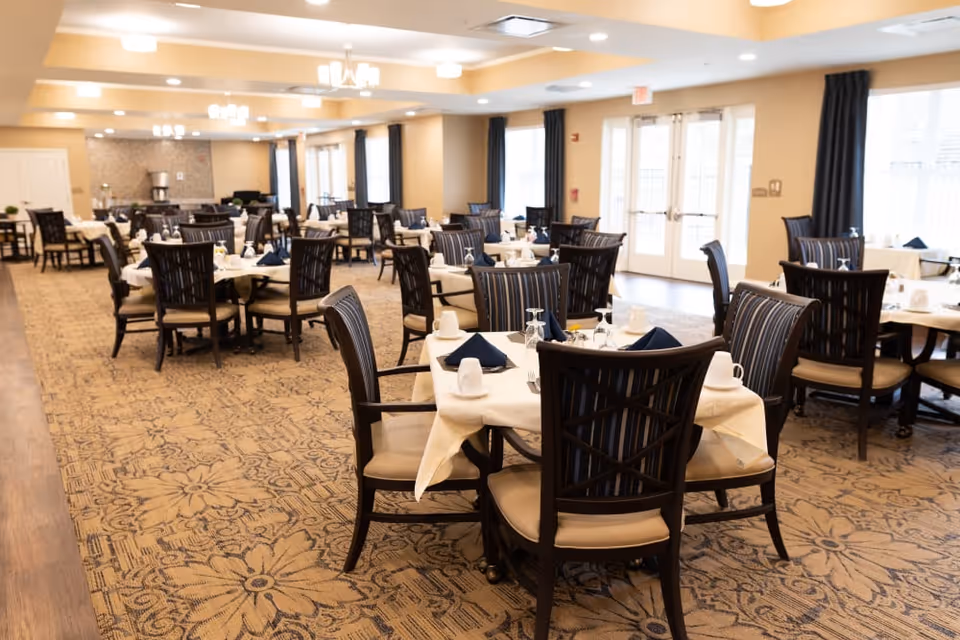 Spacious dining room with round tables set with white tablecloths, navy napkins, and wooden chairs.