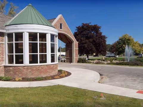 Brick senior living facility with curved glass entrance, green roof, and landscaped surroundings.