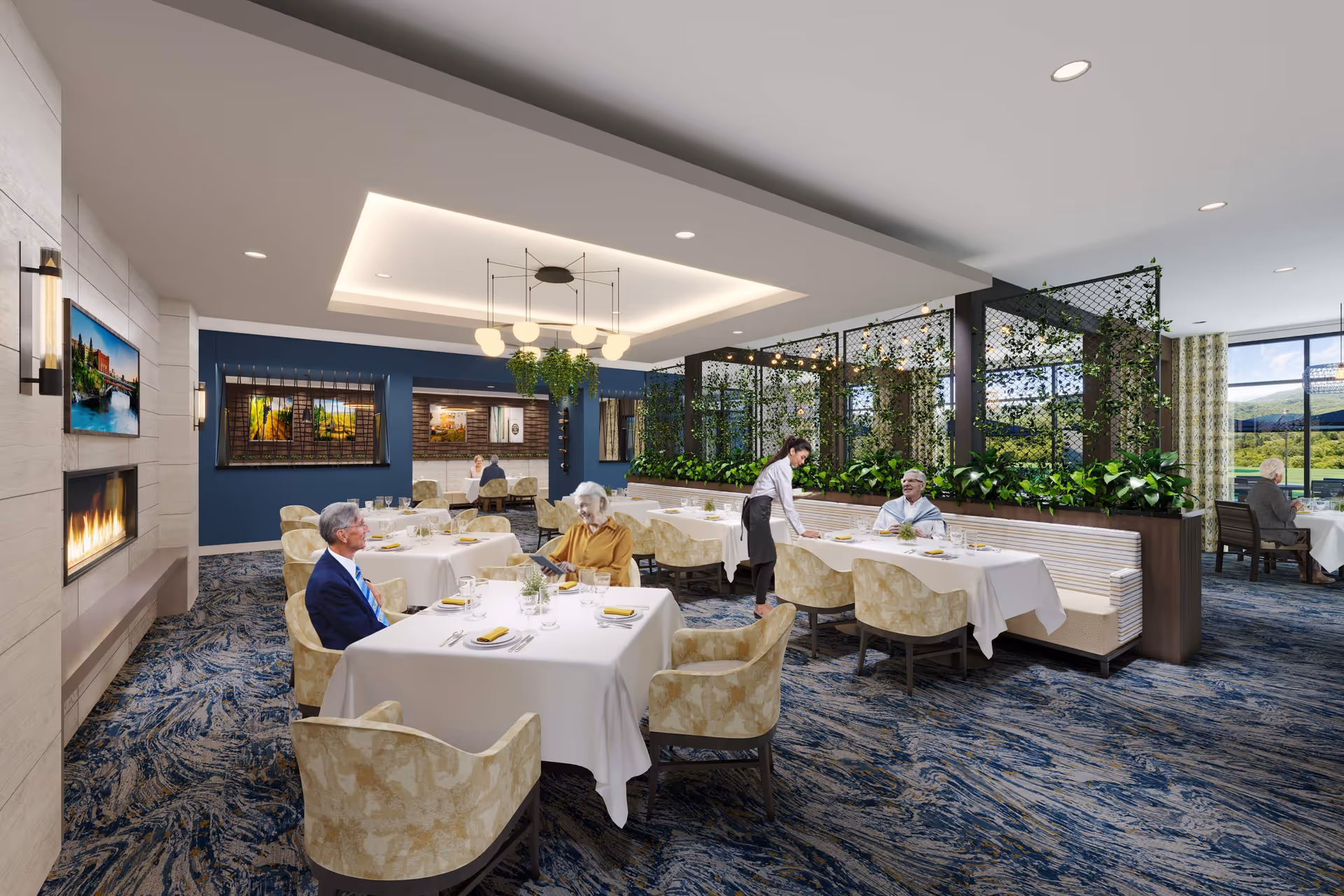 A bright and elegant dining room in a senior living facility with several tables covered in white tablecloths, beige patterned chairs, and a blue and beige carpet. There are elderly residents seated at the tables, a server attending to one table, and a fireplace with a TV mounted above it on the left wall. The room features a modern ceiling light fixture, decorative plants on a partition, and large windows showing a scenic outdoor view.