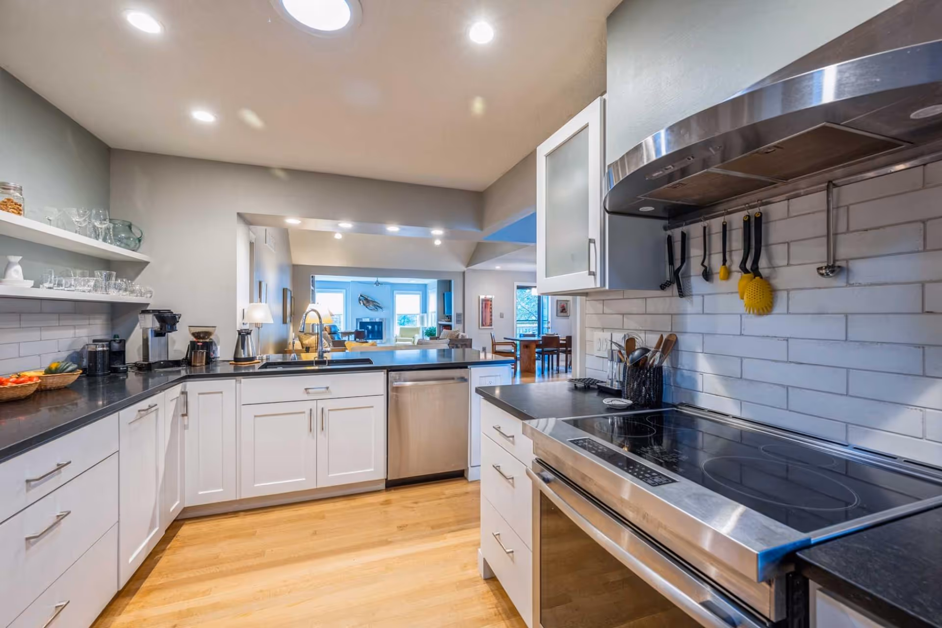 Bright modern kitchen with white cabinets, black countertops, stainless steel appliances, and an open view into the dining and living area.