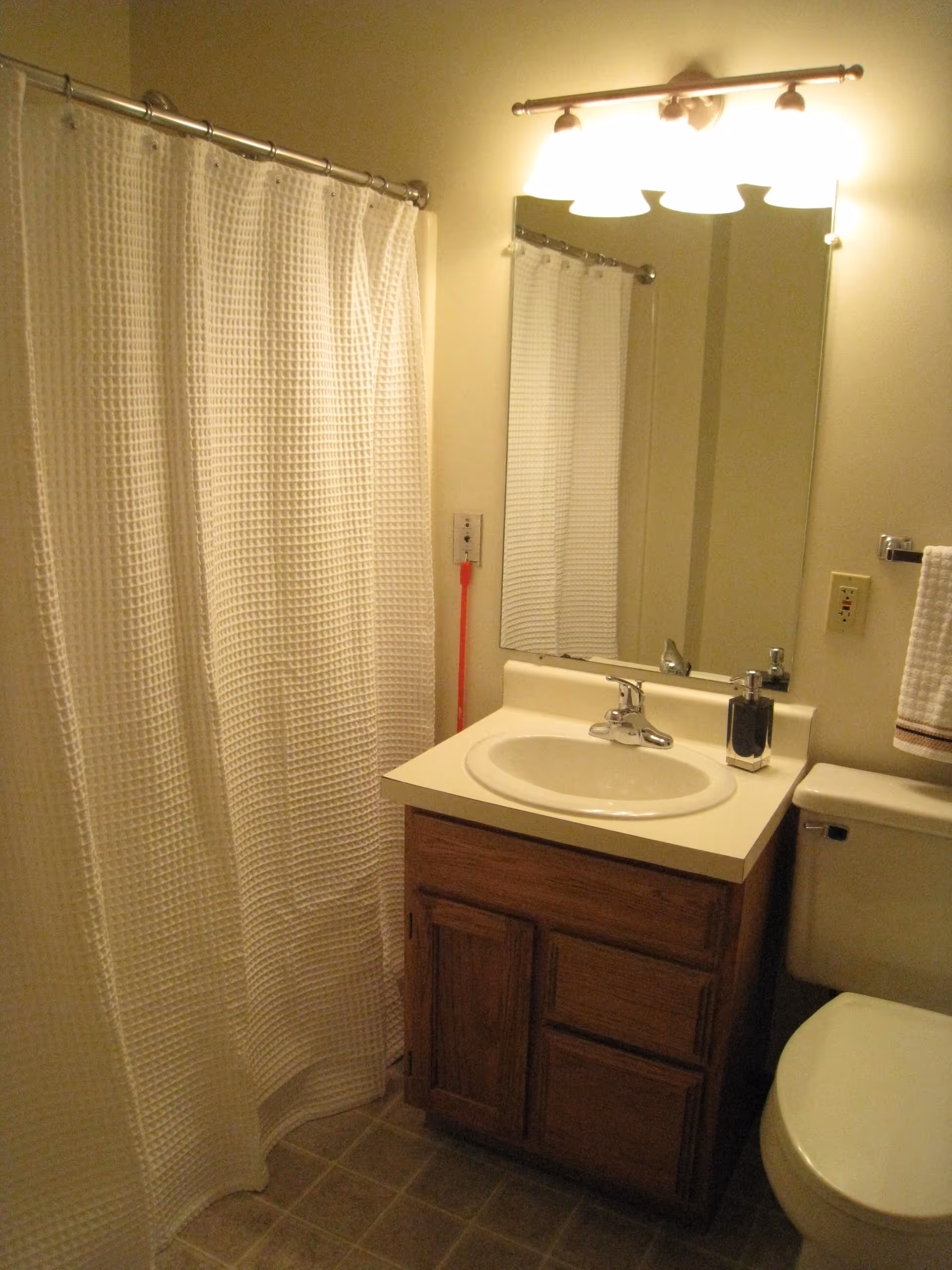 Small bathroom with a sink vanity and mirror, toilet, and a shower with a white curtain.