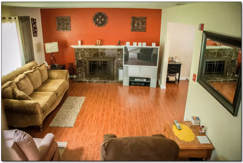 Cozy living room in a senior care home with a sofa, fireplace, TV, and wood floor.