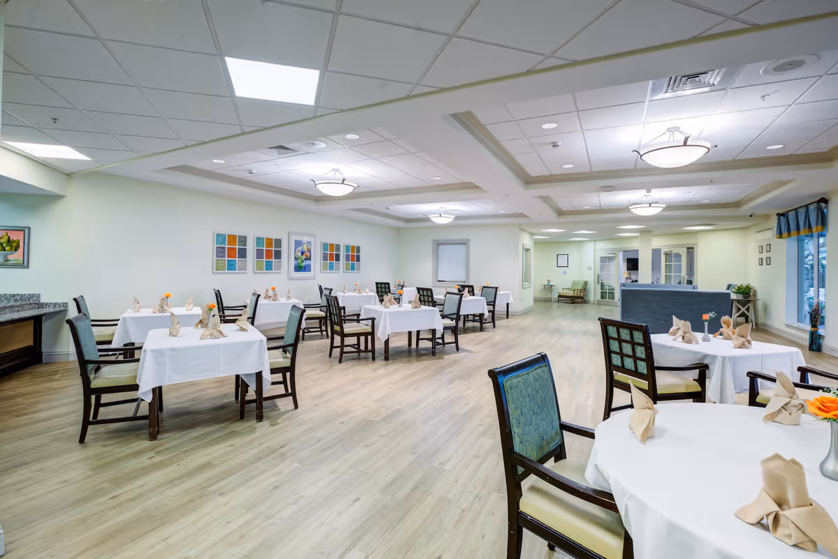 Spacious, brightly lit dining room with round and rectangular tables covered in white tablecloths and set with napkins and chairs.