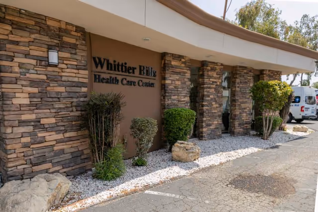 Front entrance of Whittier Hills Health Care Center with stone columns, landscaping, and a parked van.