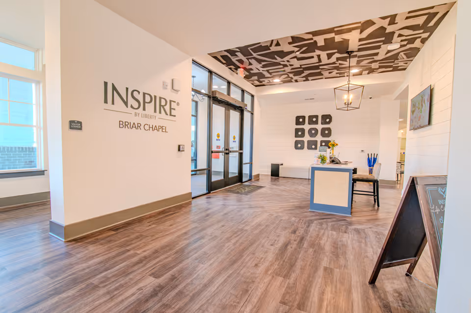 Bright, modern reception lobby of Inspire Briar Chapel with front doors, a small desk, seating, and wall signage.