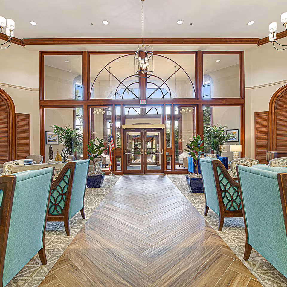 Bright lobby entrance with wood-framed glass doors, seating areas, and decorative plants.