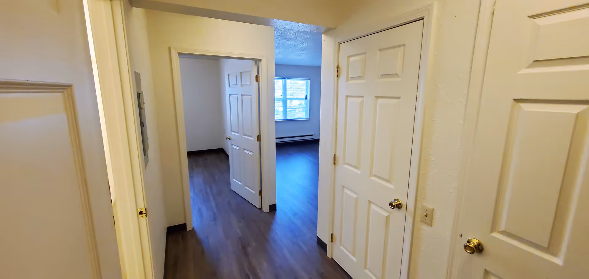Interior view of a hallway in Cougill Senior Apartments with multiple white doors and a room with a window at the end. The floor is dark wood and the walls are light-colored.
