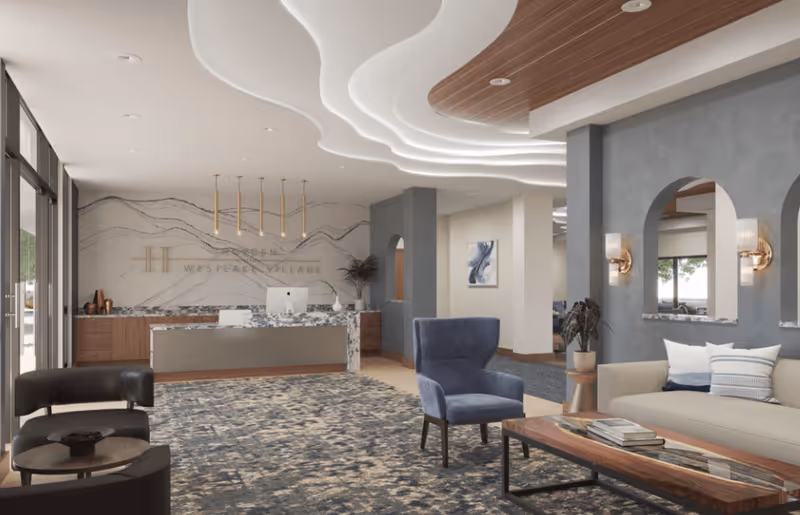 A modern and elegant reception area of The Ridge at Westlake Village featuring a marble reception desk with a computer, a patterned carpet, comfortable seating including a blue armchair and a beige sofa with pillows, decorative wall sconces, and a ceiling with artistic wave-like lighting design.