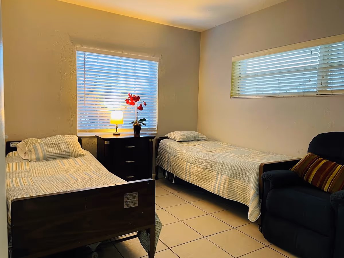 Small bedroom with two single beds, a nightstand holding a lamp and a potted orchid, and a recliner chair.