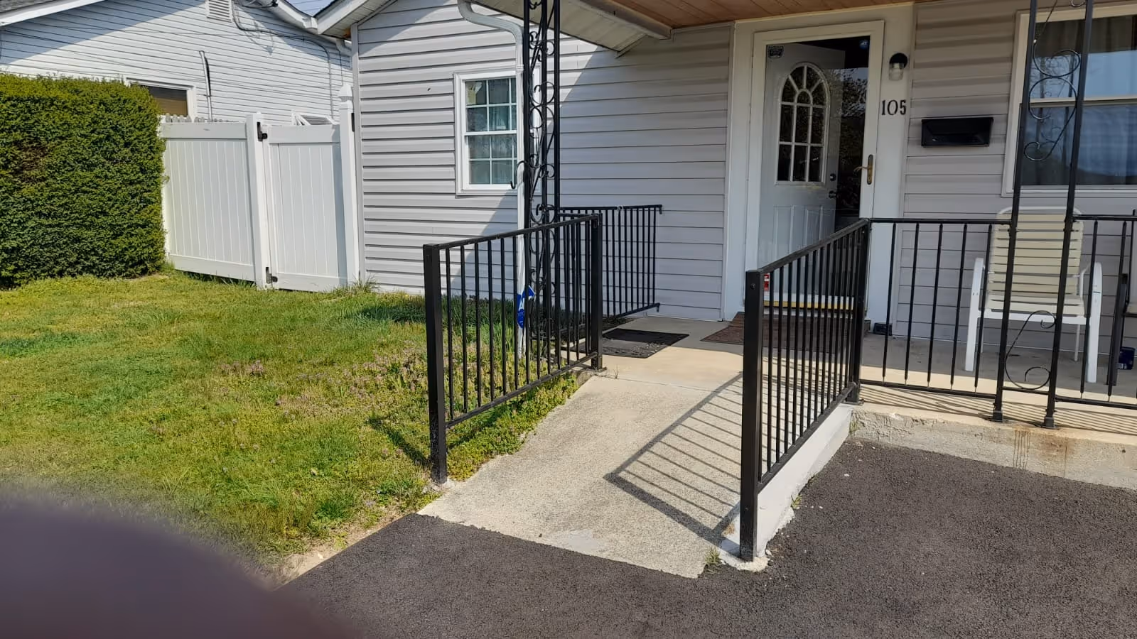 Front entrance of a single-story unit with a concrete ramp and black metal railings leading to a white door marked '105' beside a small lawn.