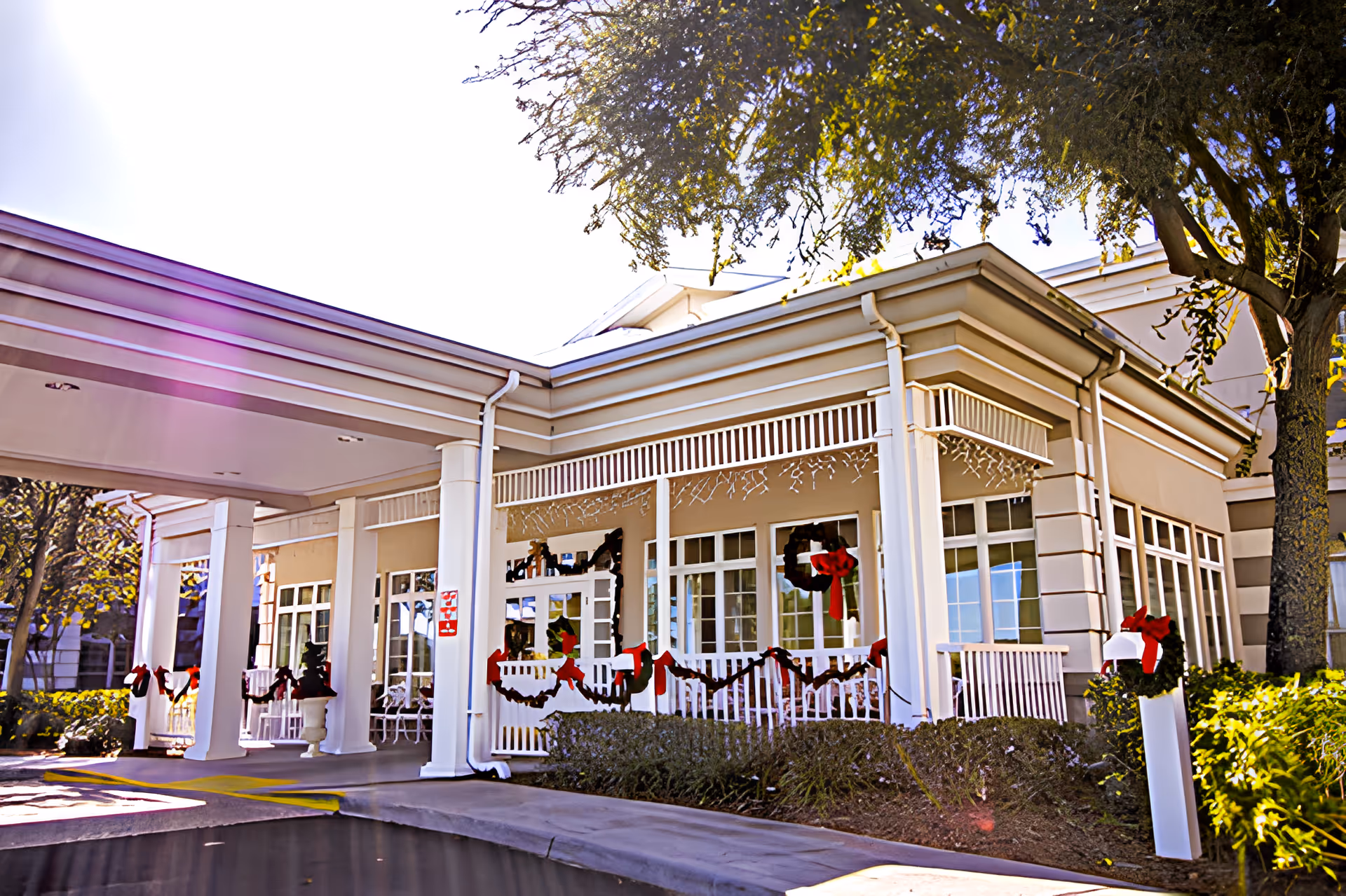 Front entrance of a senior living facility with a covered porte-cochère, columns and holiday wreaths and garlands on the railing.