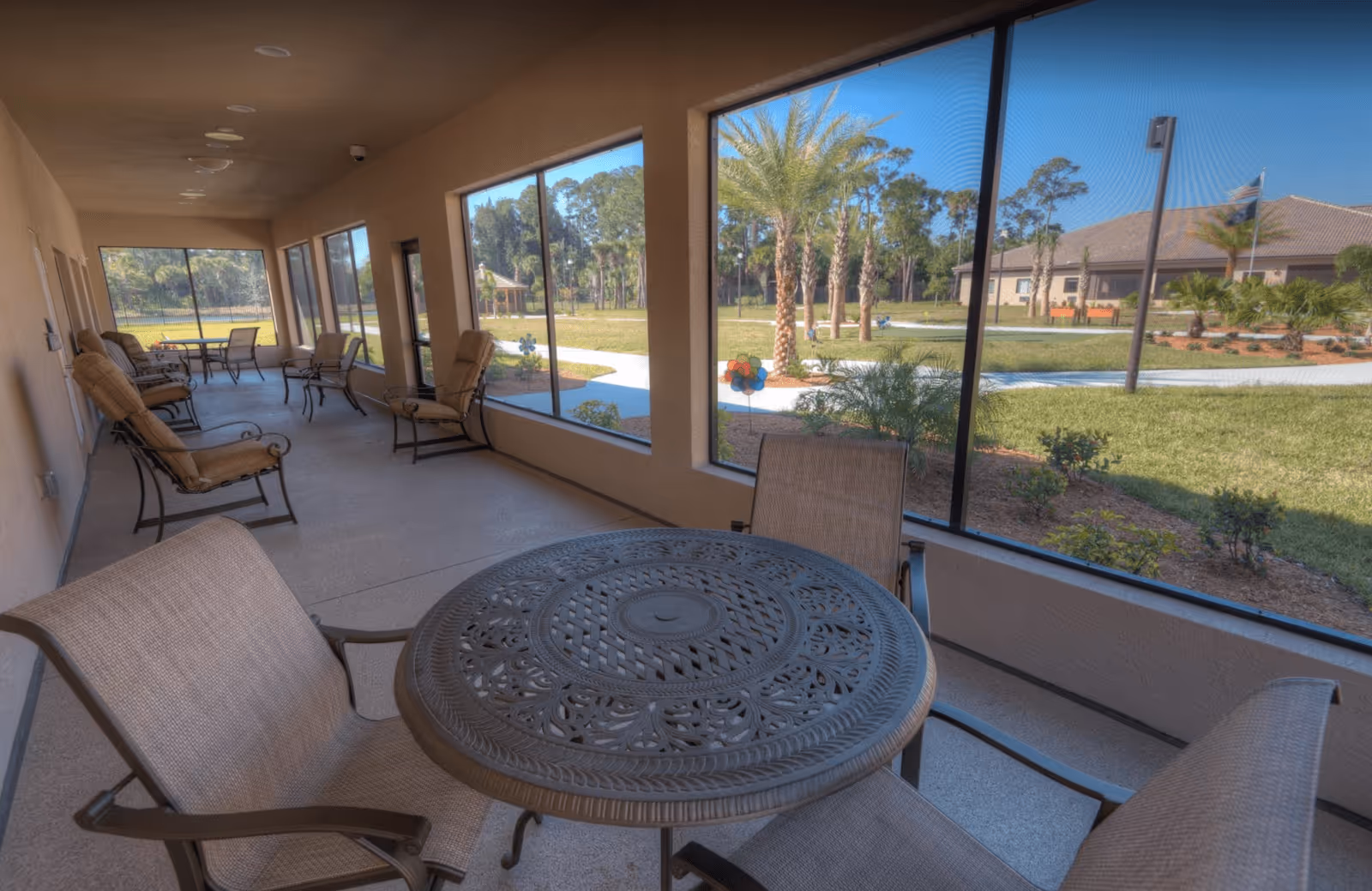 Screened porch with a round metal table and chairs overlooking landscaped grounds and palm trees.