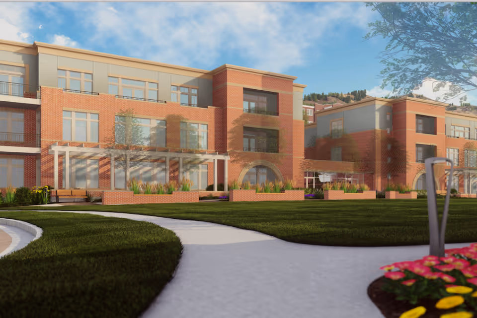 Exterior front view of a three-story brick senior living building with landscaped lawn, curved walkway, and benches.