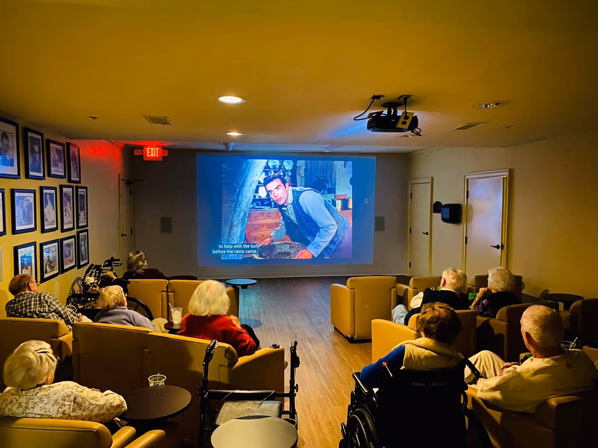 Seniors seated in a dimly lit common room watching a movie projected onto a screen.
