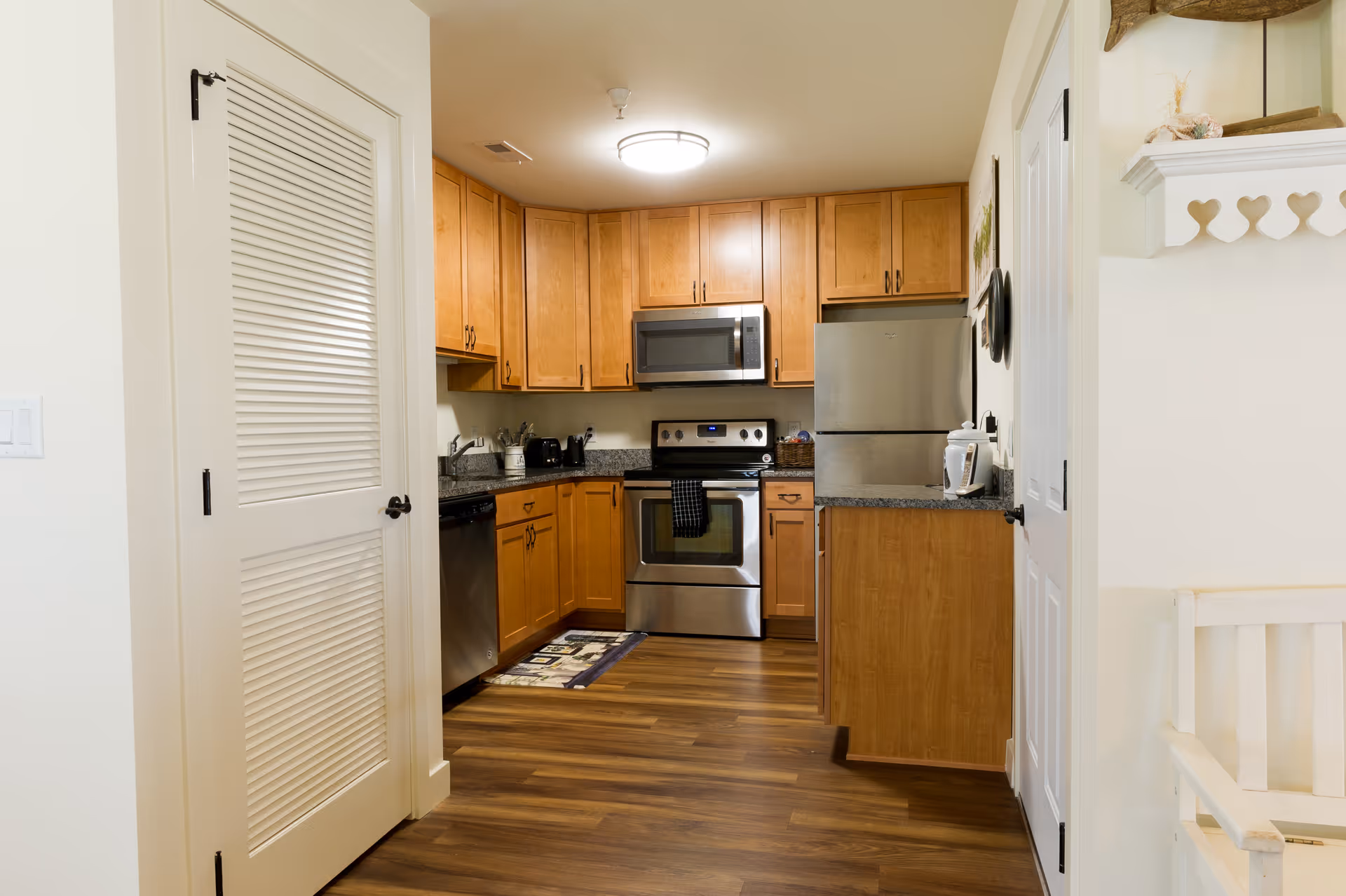 Small modern kitchen with wooden cabinets, stainless steel appliances, and wood flooring seen from an entryway.