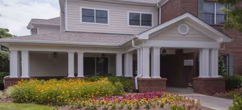 Front view of a senior living facility entrance with columns and flower beds.