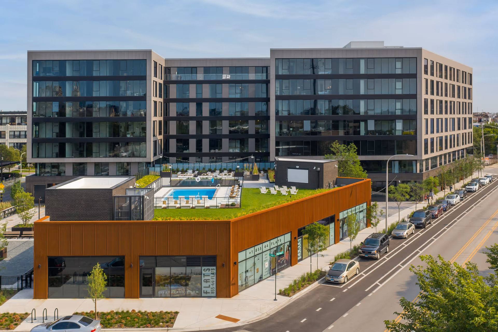 Modern multi-story residential building with a rooftop pool and ground-floor retail along a street.