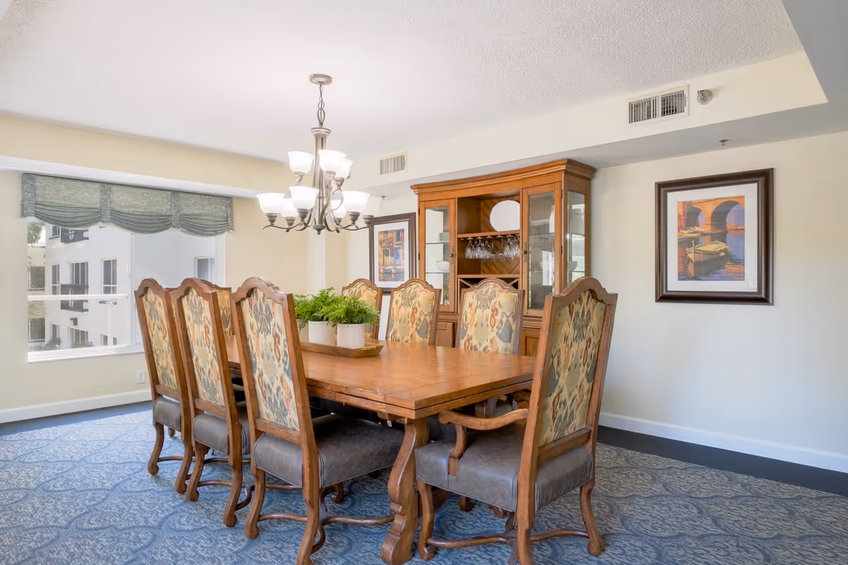 Bright dining room with a wooden table, eight upholstered chairs, a chandelier, and a china cabinet.