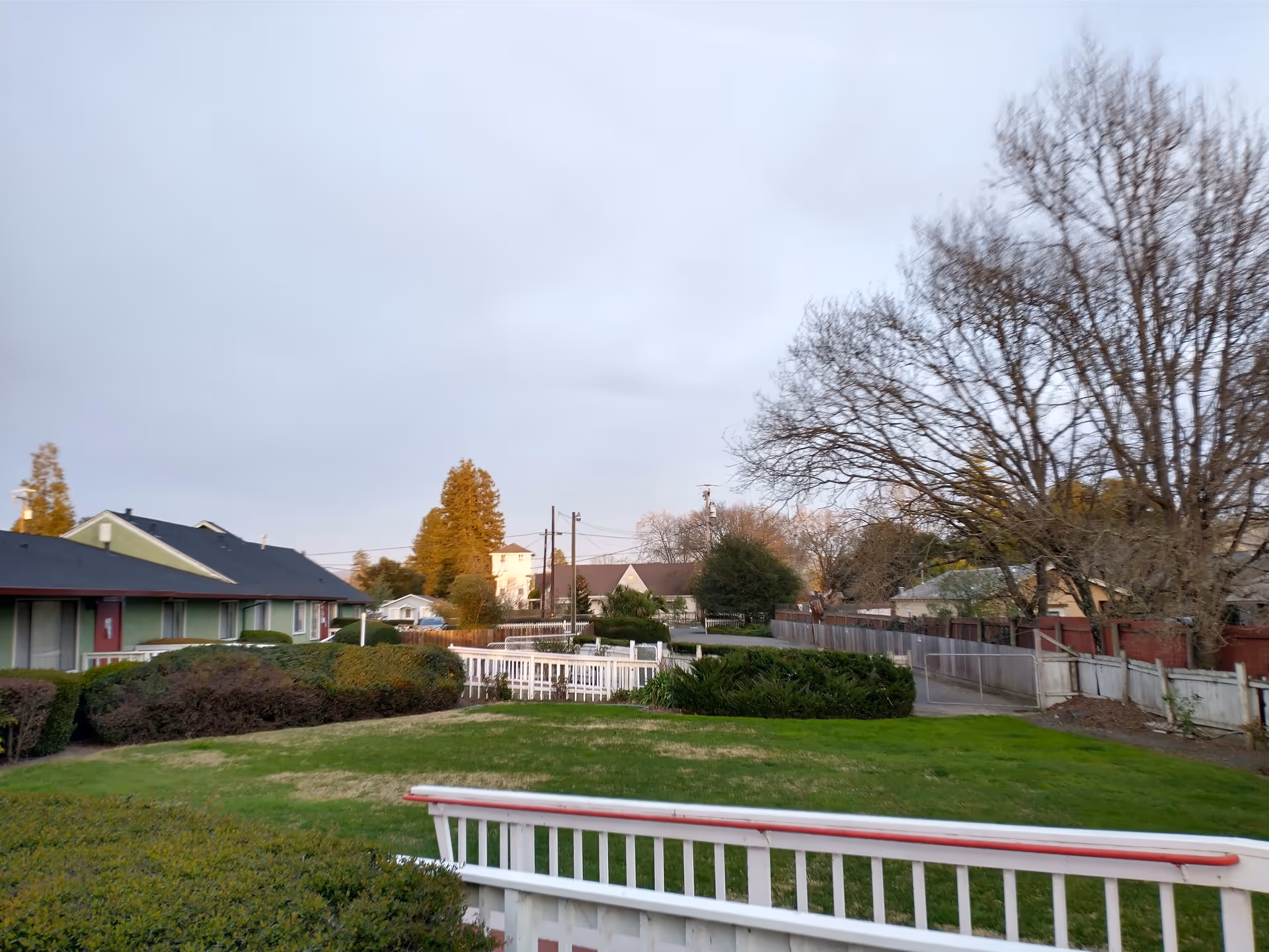 Grassy courtyard and fenced walkway at a senior living facility with low buildings and bare trees under a cloudy sky.