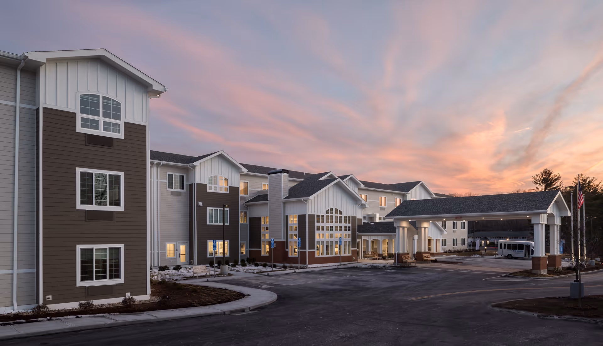 Exterior view of Charter Senior Living of Brookfield building at dusk with a partly cloudy sky. The building has multiple stories with large windows and a covered entrance area. There is a driveway and parking area in front of the building.