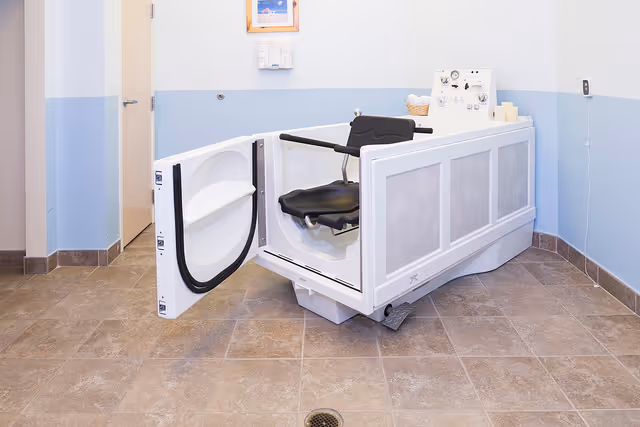 A specialized bathtub with a door and a black seat designed for assisted bathing in a clean bathroom with light blue and white walls and tiled floor.