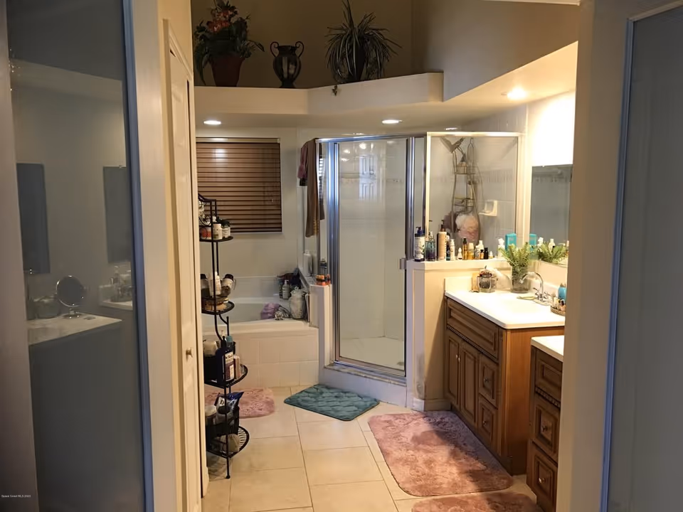 Bathroom featuring a glass-enclosed shower, bathtub, wooden vanity with sink, and shelving with toiletries.